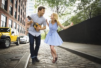 Caucasian couple playing ukulele on city street