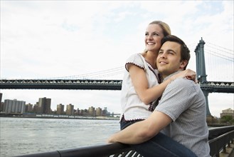 Caucasian couple hugging under Brooklyn Bridge