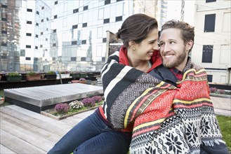 Couple wrapped in blanket on urban rooftop