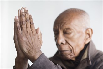 Older Black man praying with hands clasped