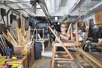 Caucasian woman working on wooden chair in workshop
