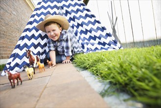 Caucasian boy wearing cowboy hat in teepee playing with toy horses