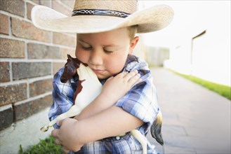 Caucasian boy wearing cowboy hat hugging toy horse