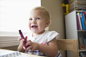 Smiling Caucasian baby girl holding crayon