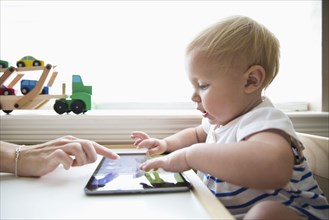 Caucasian mother helping baby girl use digital tablet