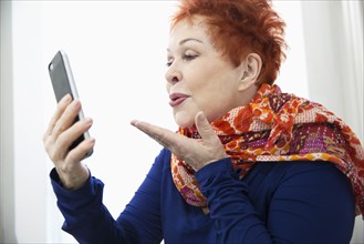 Older Caucasian woman blowing kiss at cell phone