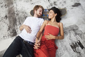 Mixed Race couple laying on rooftop with skateboard
