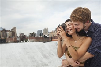 Mixed Race couple hugging on rooftop with video camera