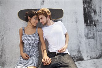 Mixed Race couple sitting on rooftop with skateboard