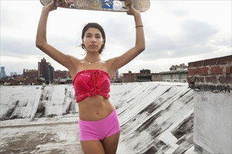 Mixed Race couple woman on rooftop holding skateboard