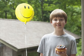Caucasian boy posing with smiley face balloon and donut