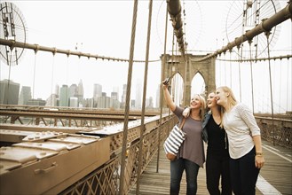 Smiling Caucasian women posing for cell phone selfie on bridge