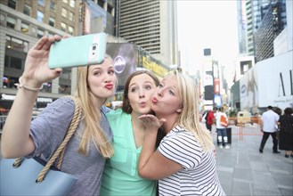 Puckering Caucasian women posing for cell phone selfie in city