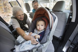 Grandmother fastening baby grandson in car seat