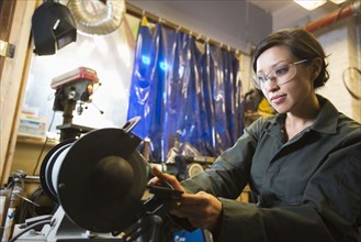 Mixed Race woman grinding metal rod in workshop