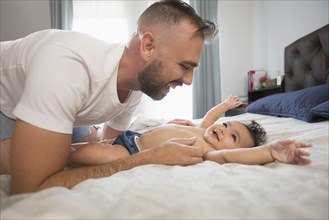 Father laying on bed playing with baby daughter