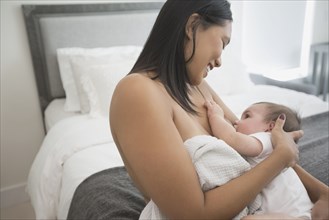 Woman sitting on bed breast-feeding baby son