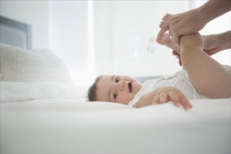 Father holding legs of baby son on bed