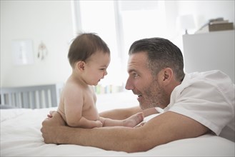 Father playing with baby son sitting on bed