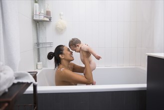 Mother sitting in bathtub holding baby son