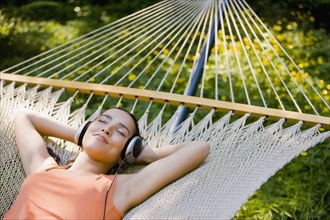 Hispanic woman laying in hammock listening to headphones