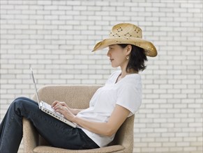 Japanese woman typing on laptop wearing cowboy hat