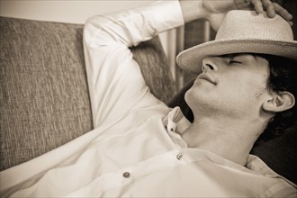 Mixed race man sleeping on sofa with hat over face