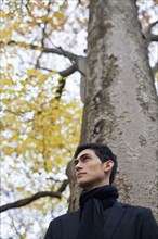 Pensive mixed race man standing under autumn tree