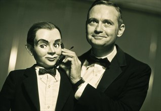Performer holding cell phone to ventriloquist dummy