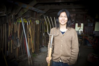 Japanese gardener holding pitchfork in barn