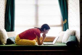 Japanese woman leaning on day bed reading laptop