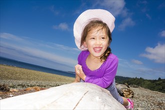 Smiling girl laying on driftwood log at beach