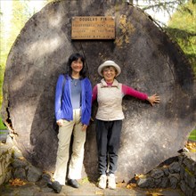 Smiling Japanese mother and daughter posing at tree stump
