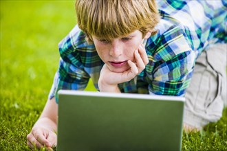 Caucasian boy kneeling in grass using laptop
