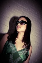 Glamorous Asian girl wearing sunglasses near brick wall