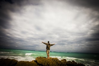 Caucasian man standing on rocks at ocean with arms outstretched