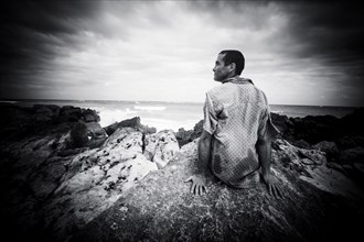 Pensive Caucasian man sitting on rocks at ocean