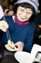 Older Japanese woman eating food with chopsticks