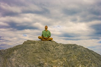 Man meditating on rock under clouds