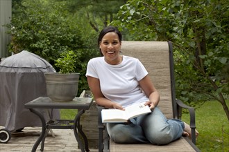 African American woman reading book in back yard