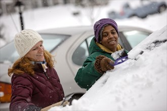 Two women scraping snow from windshield