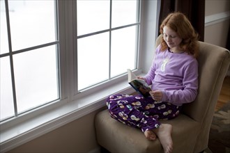 Caucasian girl reading on book near window