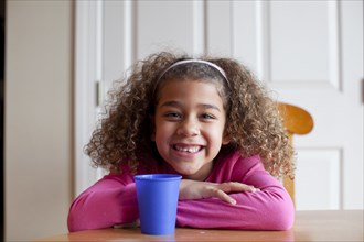 Grinning mixed race girl sitting with cup