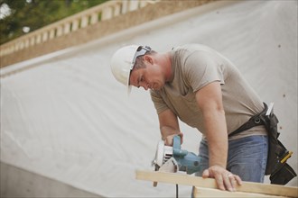 Caucasian construction worker sawing wood planks