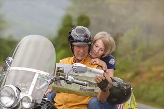 Older Caucasian couple reading map on motorcycle