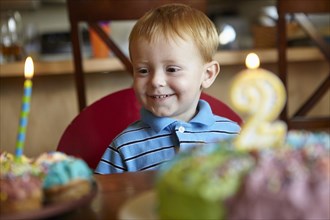 Caucasian boy admiring birthday cake and cupcake