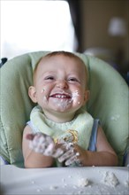 Caucasian baby eating cake in high chair
