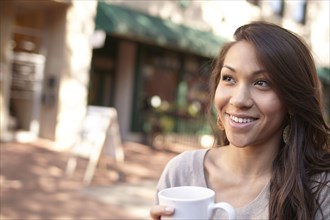 Mixed race woman drinking coffee on sidewalk
