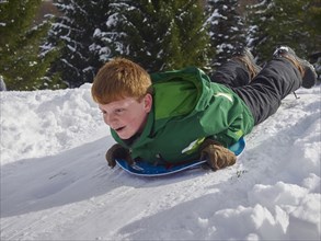 Caucasian boy sledding on snowy hill