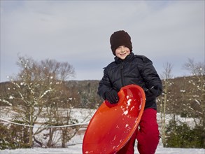 Caucasian boy holding sled on snowy hill